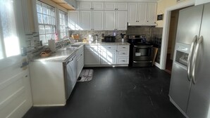 A kitchen with white cabinets, a stainless steel refrigerator, a microwave, and a stove. - Escape in Bossier Family & Work-Friendly (Bossier City)