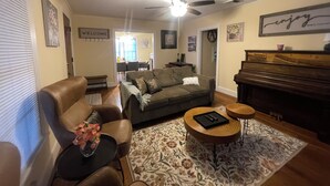 A living room with a sofa, a coffee table, a piano, and a ceiling fan. - Escape in Bossier Family & Work-Friendly (Bossier City)