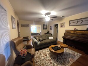 Ein Wohnzimmer mit einer Couch, einem Couchtisch, einem Klavier und einem Deckenventilator.