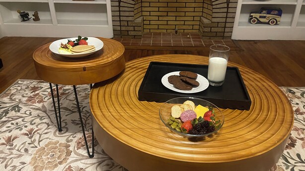 A dining area with a brick fireplace, a round wooden table with a tray of cookies and a glass of milk, and a plate of pancakes. - Escape in Bossier Family & Work-Friendly (Bossier City)