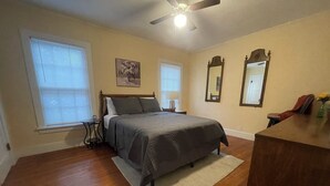 A bedroom with a bed, two windows, a ceiling fan, a bedside table, and a dresser. - Escape in Bossier Family & Work-Friendly (Bossier City)