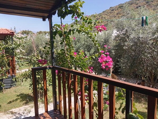 Una terraza de madera con barandilla, rodeada de exuberante vegetación y plantas en flor.