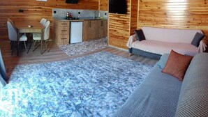 A cozy cabin interior with a wooden interior, a dining area with chairs and a table, a kitchenette, and a sofa with cushions. - Riviera bungalov apart (Demre)