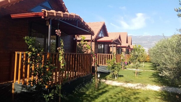A row of wooden cabins with balconies, a grassy yard, and a mountainous backdrop. - Riviera bungalov apart (Demre)