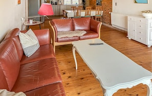 Una sala de estar con un sofá de cuero marrón, una mesa blanca y una cocina al fondo.