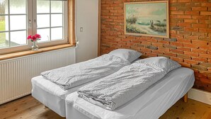 A room with a bed, a window with a view, a painting on the wall, and a brick wall.