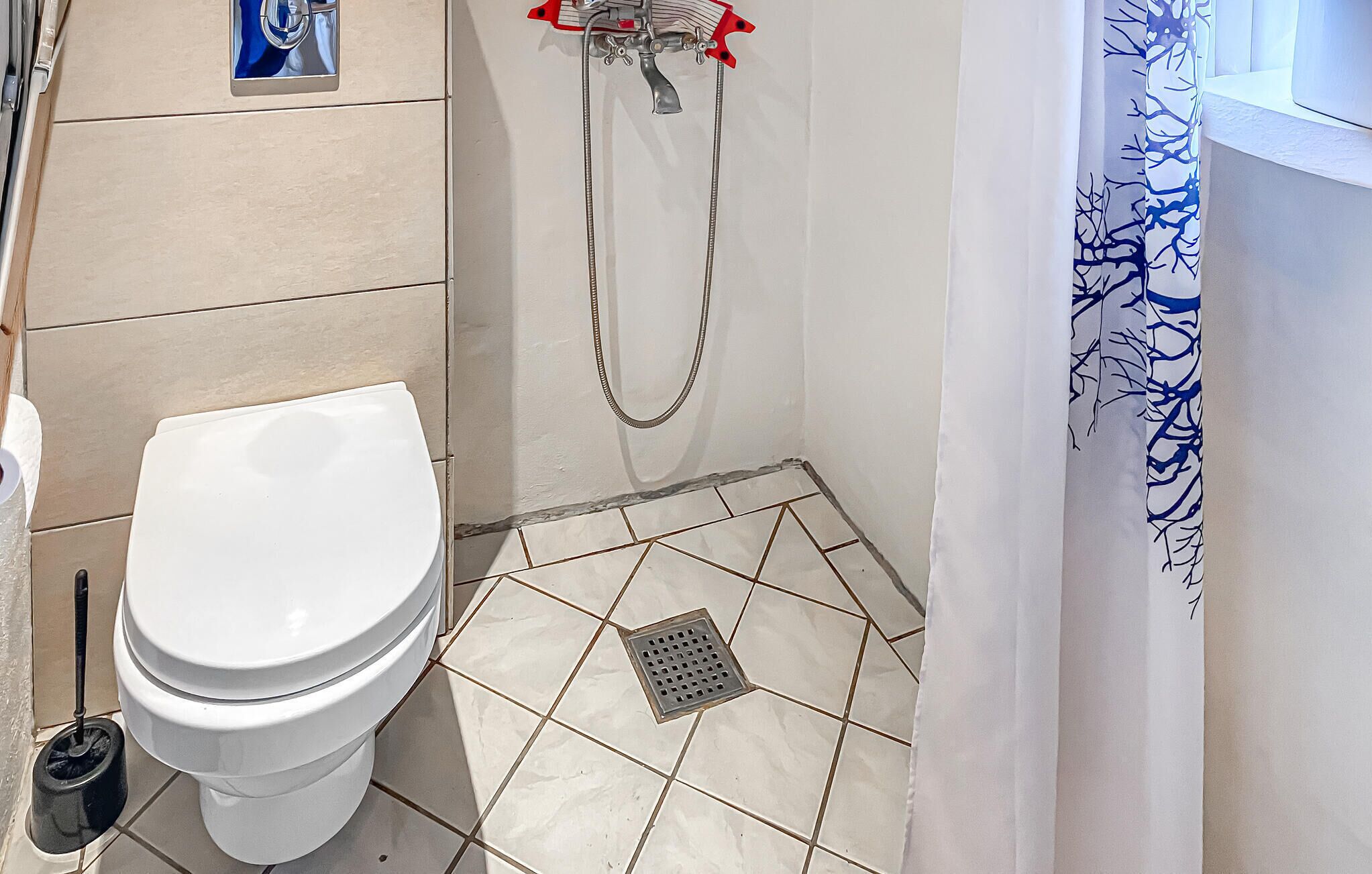 A bathroom with a toilet, a shower, and a window with a curtain.