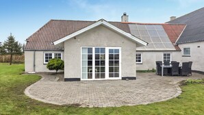 A house with a paved patio, a small covered area with a table and chairs, and a large window.
