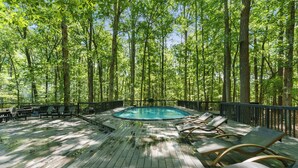 A wooden deck with a pool and lounge chairs, surrounded by trees.