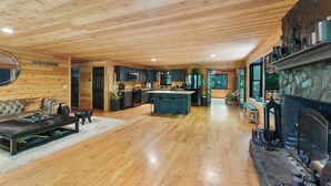 A spacious living area with a wooden ceiling, a fireplace, and a kitchen in the background.