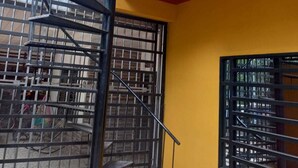 A spiral staircase with metal railings, a yellow wall, and a window with metal bars.