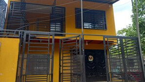A yellow building with a black gate and a red awning.
