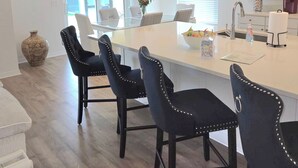 Una cucina moderna con isola centrale, sedie imbottite nere, illuminazione a sospensione e un'area pranzo con un'ampia finestra.