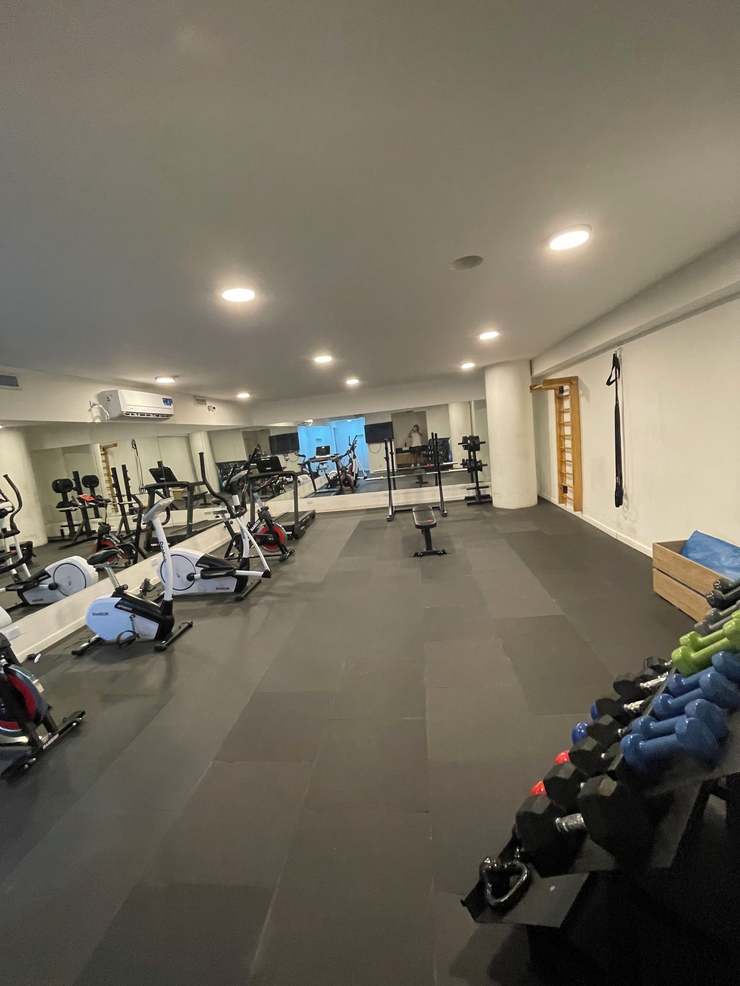 Ein Fitnessraum mit verschiedenen Trainingsgeräten, einem Spiegel und einer Holallee.