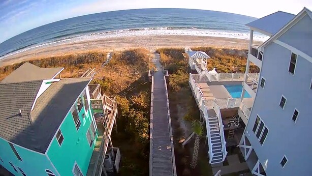 Un hotel frente al mar con piscina, terraza de madera y vistas al océano.