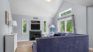 Een moderne woonkamer met een open haard, een groot raam met gordijnen, een bank en een televisie.
