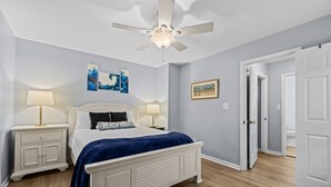 Een slaapkamer met een bed, twee nachtkastjes met lampen, een plafondventilator en een deur naar een andere kamer.