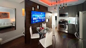 Una cocina moderna con televisor de pantalla plana, electrodomésticos de acero inoxidable y un comedor con mesa de vidrio y sillas blancas.
