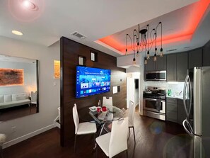 A modern kitchen with a flat-screen TV, stainless steel appliances, and a dining area with a glass table and white chairs. - Downtown DC Rowhouse Apartment 3-Bedroom Suite-A (Washington)