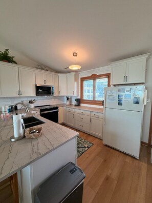 A modern kitchen with white cabinets, a stainless steel sink, a microwave, and a refrigerator. - Oceanfront 4BR Retreat with Private Beach Access-Discounted for weeks of 6/7 & 6 (Emerald Isle)
