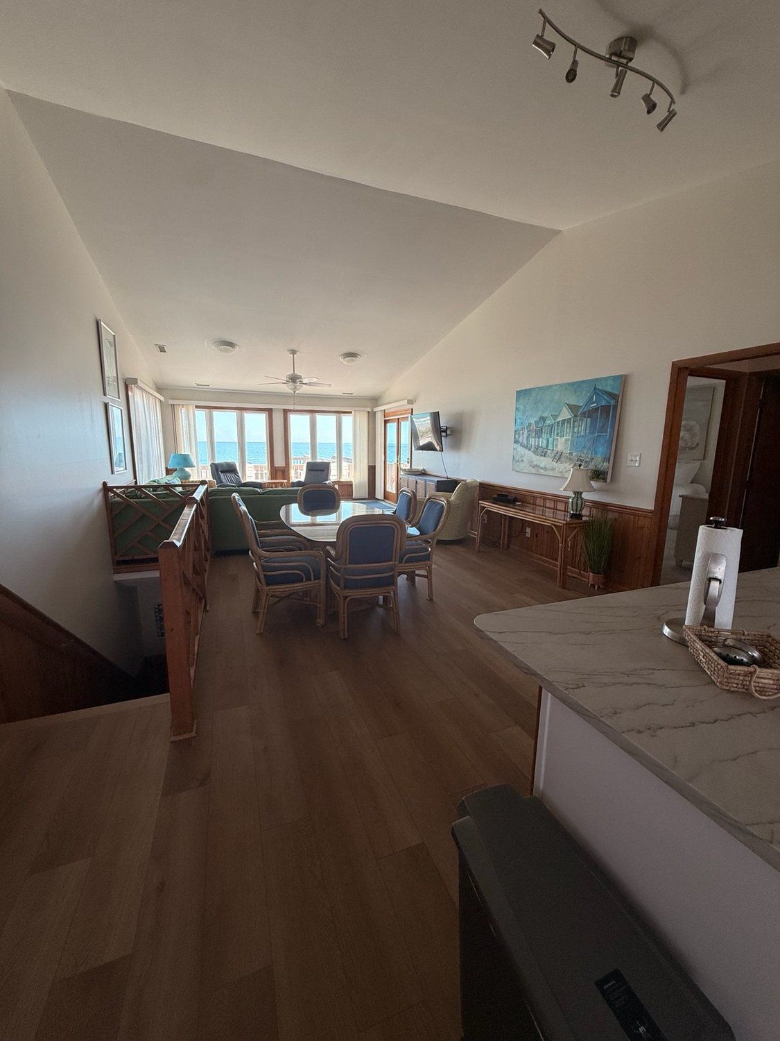 A spacious living area with a dining table, chairs, a pool table, and a large window overlooking the sea.