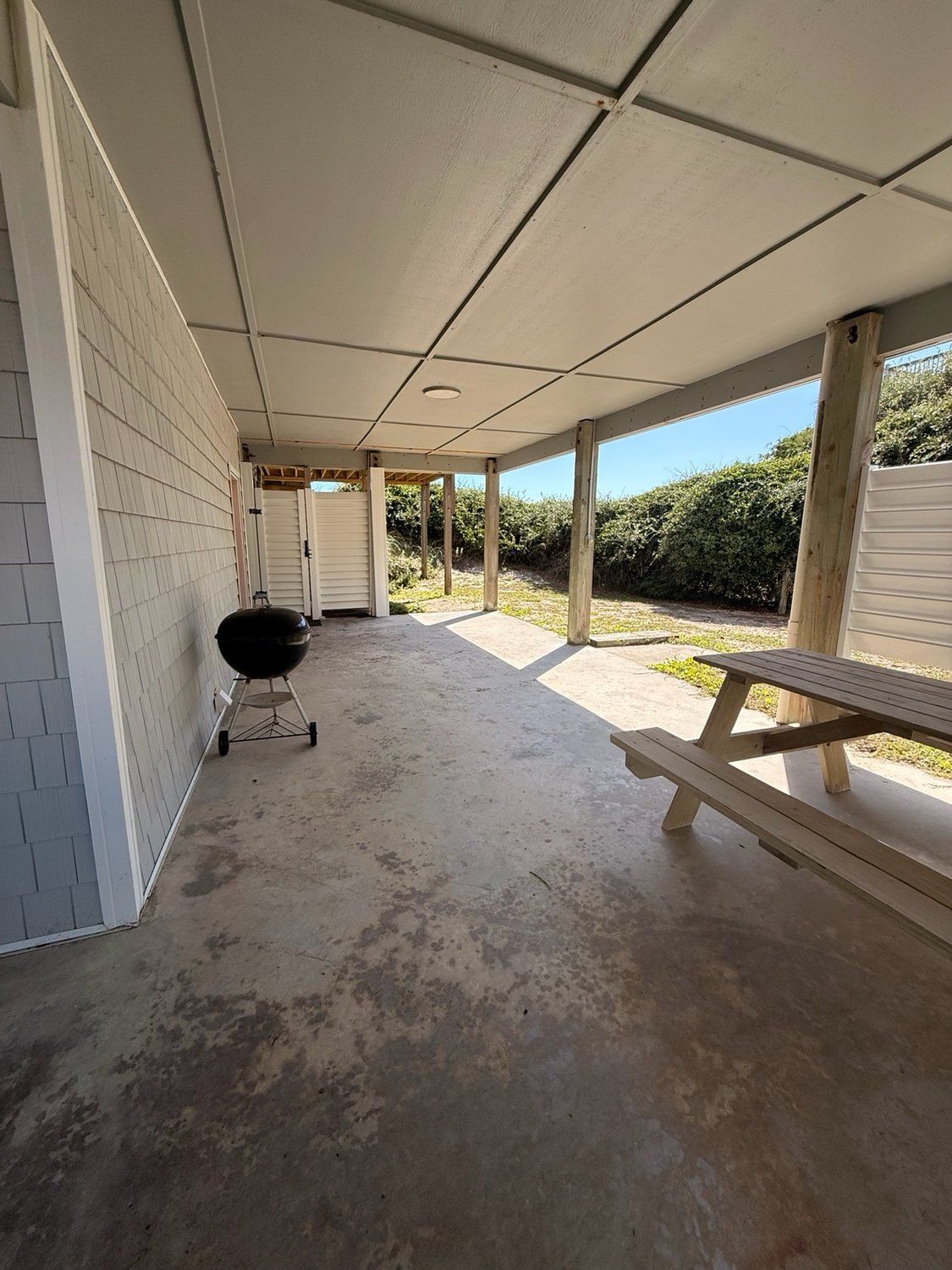 A covered outdoor area with a concrete floor, a barbecue grill, and a picnic table.