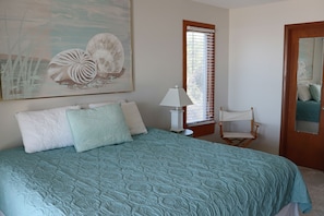 A bedroom with a bed, pillows, a lamp, a chair, a window, and a painting. - Oceanfront 4BR Retreat with Private Beach Access-Discounted for weeks of 6/7 & 6 (Emerald Isle)