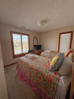 A bedroom with two beds, a dresser, a mirror, and windows with blinds. - Oceanfront 4BR Retreat with Private Beach Access-Discounted for weeks of 6/7 & 6 (Emerald Isle)