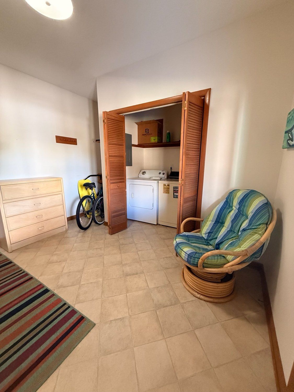 A compact living space with a bed, a chair, a washing machine, and a bicycle.