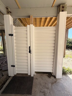 A closed white gate with a metal handle, a concrete floor, and a wooden ceiling structure. - Oceanfront 4BR Retreat with Private Beach Access-Discounted for weeks of 6/7 & 6 (Emerald Isle)