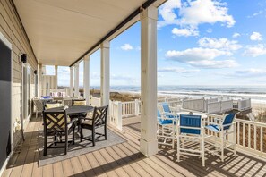 Eine überdachte Terrasse im Freien mit Tisch und Stühlen, mit Blick auf einen Strand.