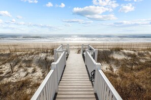 Ein Holzsteg führt zu einem Strand unter blauem Himmel.