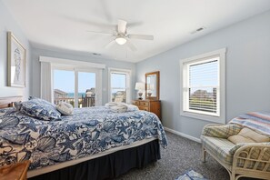 Une chambre à coucher comprenant un lit, un ventilateur de plafond, une table de chevet, une lampe, une chaise et de grandes fenêtres donnant sur un beau paysage.