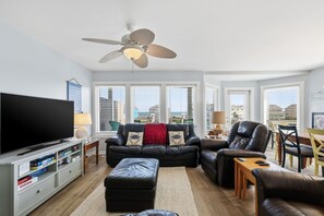 Un salon équipé d’un téléviseur à écran plat, d’un ventilateur de plafond, d’un canapé, d’une table basse et d’un coin repas avec des chaises et une table.