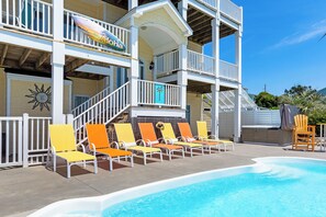 A pool area with lounge chairs, a lifeguard stand, and a building with balconies. - Spacious 6BR OF Home, Elevator & Pool (Emerald Isle)