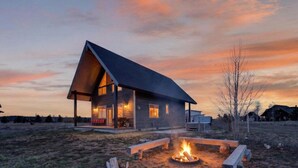 Een modern huis met een overdekte veranda, een vuurkorf en een helder uitzicht op het omliggende landschap.