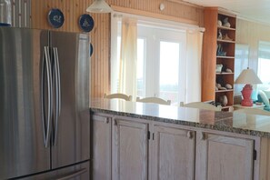 Eine Küche mit Edelstahl-Kühlschrank, Holzschränken, einer Granit-Arbeitsplatte und Blick durch ein Fenster.