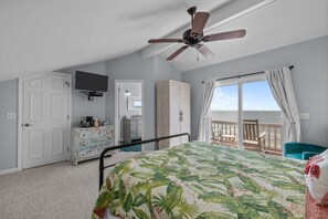 Et soveværelse med seng, ventilator, fjernsyn, garderobeskab, kommode, balkon med stol og havudsigt.