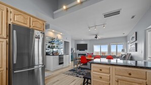 A modern kitchen with a stainless steel refrigerator, wooden cabinets, and a dining area with red chairs. - 4 BD| 4.5 Bath| Luxury Oceanfront Escape-Discounted week of 8/15 (Emerald Isle)