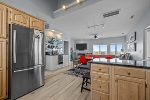 A modern kitchen with a stainless steel refrigerator, wooden cabinets, and a dining area with red chairs. - 4 BD| 4.5 Bath| Luxury Oceanfront Escape-Discounted weeks for June & August (Emerald Isle)