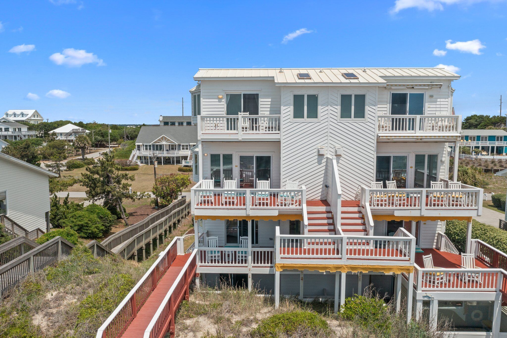 Una casa frente a la playa con varios pisos, balcones, un porche cubierto y una terraza de madera.