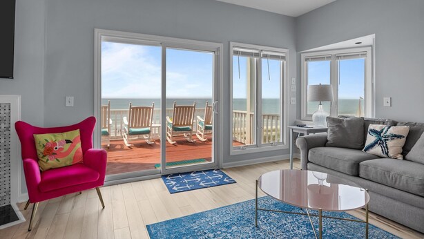 A living room with a bright view of the ocean, a pink chair, a gray sofa, and a coffee table. - 4 BD| 4.5 Bath| Luxury Oceanfront Escape-Discounted week of 8/15 (Emerald Isle)