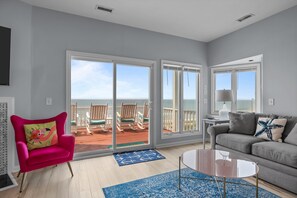 Un salon avec une vue dégagée sur l’océan, un fauteuil rose, un canapé gris et une table basse.