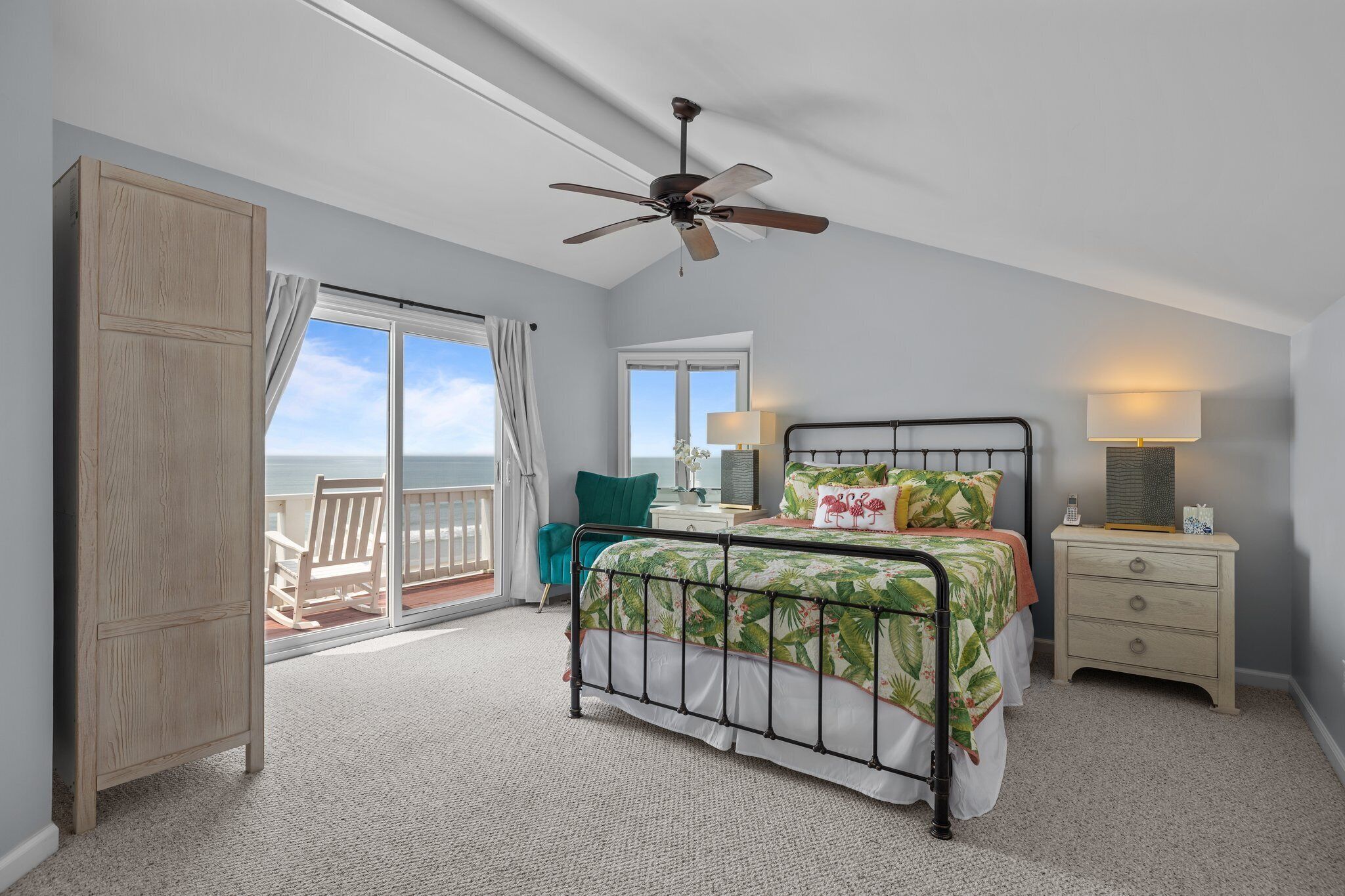 A bedroom with a bed, a nightstand, a ceiling fan, a window with a view, and a door.