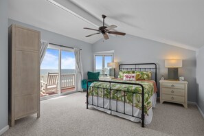 A bedroom with a bed, a nightstand, a ceiling fan, a window with a view, and a door. - 4 BD| 4.5 Bath| Luxury Oceanfront Escape-Discounted weeks for June & August (Emerald Isle)