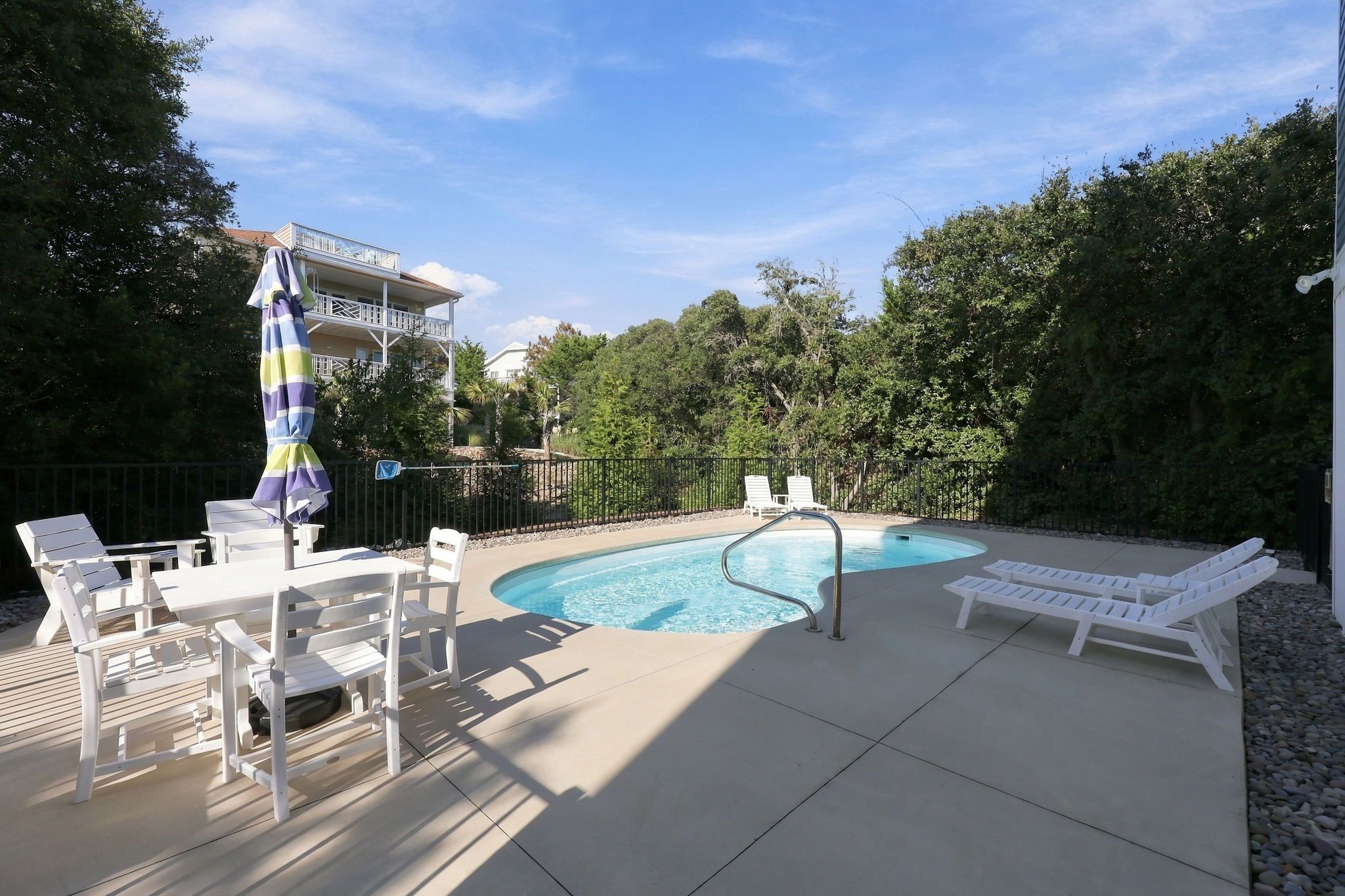 A swimming pool with lounge chairs and a table, surrounded by trees and a building with a balcony.
