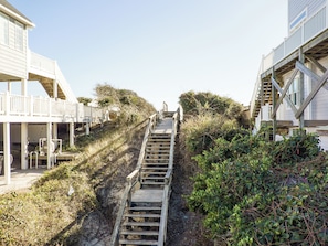 A wooden staircase leading up a sandy slope, surrounded by vegetation and adjacent to a building with a balcony. - Second Row Ocean View Retreat w/ Pool and Elevator (Emerald Isle)