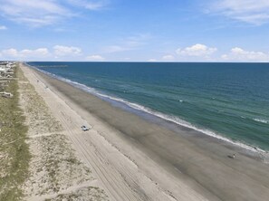 Une plage avec un ciel dégagé, un rivage sablonneux et une jetée visible au loin.