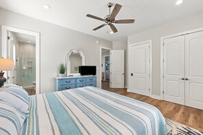 Ein Schlafzimmer mit einem Bett, einem Schminktisch, einem Fernseher und einem Deckenventilator.