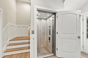 Ein modernes Interieur mit einer Holztreppe, einer weißen Tür und einem Metallaufzug.